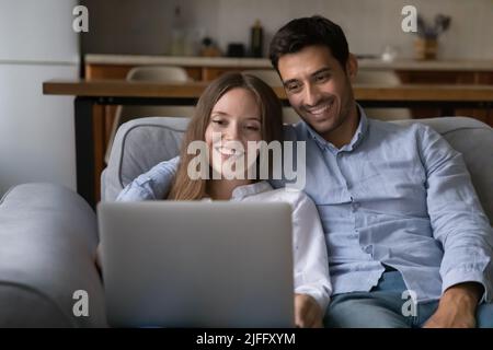Le coppie trascorrono il tempo libero a casa riposandosi sul divano con un computer portatile Foto Stock