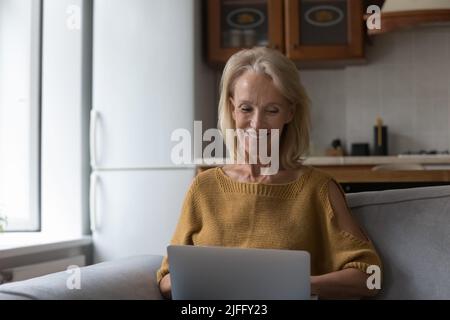 Sorridente donna anziana che usa un notebook a casa Foto Stock