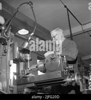 Officina meccanica nel 1940s. Un uomo anziano visibilmente un simbolo di qualità e conoscenza in una macchina tagliaperni, formando un pezzo di metallo in una parte utile per una macchina o un'auto. La lampada vista sopra la macchina è stata progettata dall'inventore svedese Johan Petter Johansson, 1853-1943, l'uomo dietro la chiave regolabile e la chiave per tubi. La lampada è chiamata Triplex-pendle ed è stata introdotta nelle industrie per migliorare le condizioni di lavoro nelle fabbriche. Svezia 1946 Kristoffersson Ref X137-6 Foto Stock