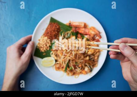 Tenere a mano i bacchetti con il pasto sopra il piatto. Uomo che mangia Pad Thai cibo in strada ristorante. Foto Stock