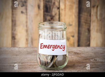 Monete in vaso di vetro con etichetta di emergenza, concetto finanziario. Sfondo in legno vintage Foto Stock