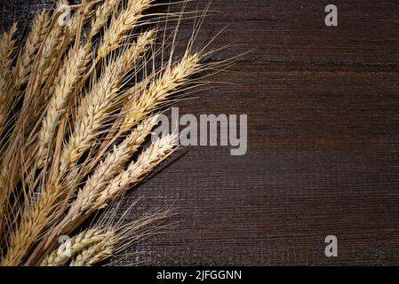 Le orecchie di fondo di grano giacciono su grani dorati di grano sparsi su una tavola di legno. Foto Stock