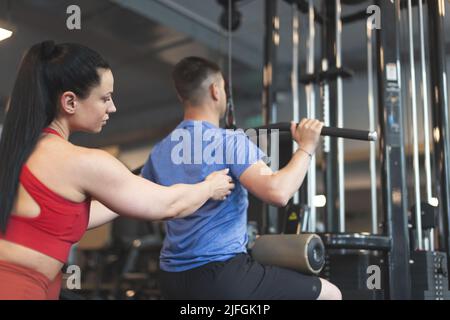 Giovane allenatore personale caucasico donna in abbigliamento sportivo aiuta a cliente sulla stazione palestra di regolazione indietro Foto Stock