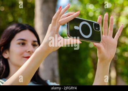 Giovane donna bruna con tee turchese e cortina arancione sul parco della città, all'aperto scattare foto orizzontali con il suo smartphone. Foto Stock