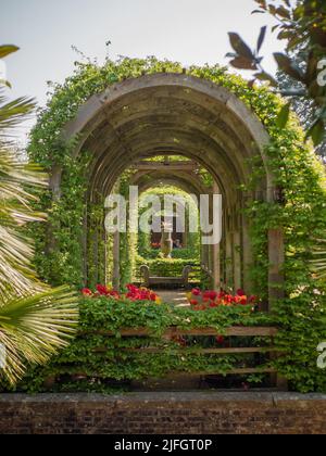 Un colpo verticale di arco in pietra circondato da fiori e foglie nel parco del castello di Arundel Foto Stock
