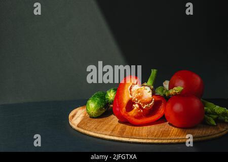 rami di asparagi verdi freschi, peperoni, pomodori e cetrioli su un asse di legno, sfondo grigio scuro, vista dall'alto. Concetto di tendenza di base con spazio di copia Foto Stock