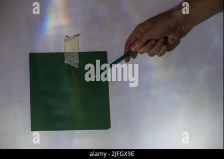 La mano dell'uomo maturo punta al pezzo di carta con la matita. Pezzo di carta verde quadrato vuoto fissato alla parete. Una luce astratta e un'ombra che disegnano su un Foto Stock