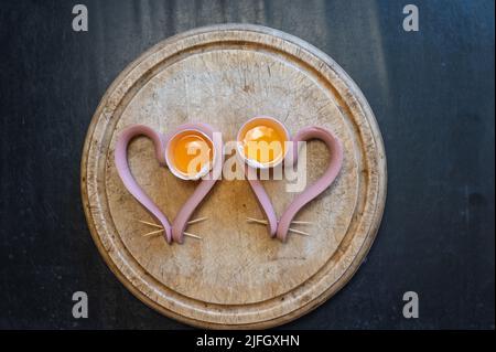 Due salsicce a forma di cuore giacciono su un tagliere. I tuorli crudi pollo nei gusci d'uovo si trovano fianco a fianco. Cottura del pasto. Amore, concetto di relazione. SEL Foto Stock