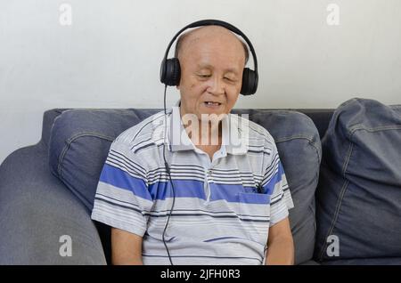 uomo anziano che ascolta musica con le cuffie sul divano. Foto Stock