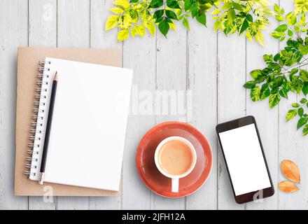 Vista dall'alto, notebook aperto, smartphone, matita e tazza di caffè su sfondo rustico bianco tavolo di legno. Accogliente colazione autunnale. Elenco benna anticaduta. Disposizione piatta Foto Stock