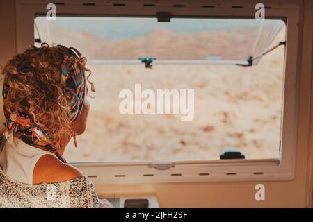 Vista posteriore della donna che viaggia guardando fuori dalla finestra del camper. Vita dei furgoni e stile di vita delle persone di viaggio. Libertà di vivere fuori dalla griglia in un veicolo e alte Foto Stock