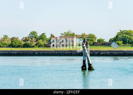Casa abbandonata e rotta nella laguna di Venezia, e tre grandi pali di legno impiantati nel fondale chiamato Briccola o Bricola (Dolphin), Italia. Foto Stock