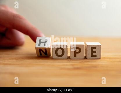 Concetto di speranza o nope. Il dito capovolge la lettera al cubo di legno cambiando la parola nope alla speranza. Messaggio per la modifica dal pessimismo all'ottimismo, negativo Foto Stock