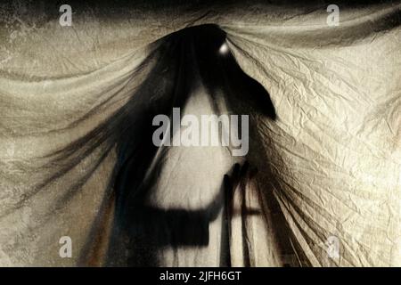Un orrore spaventoso di una figura demoniaca che si staglia dietro un sipario. Con occhi luminosi. Con una modifica grunge. Foto Stock