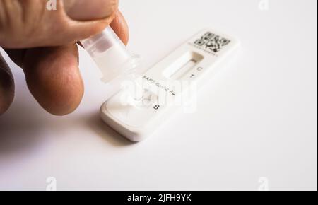 Un campione di tampone di covid in soluzione viene gocciolato sulla cassetta di prova di un test FlowFlex Lateral Flow o Rapid Antigen Foto Stock