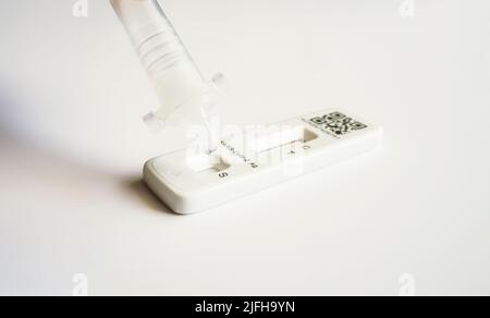 Un campione di tampone di covid in soluzione viene gocciolato sulla cassetta di prova di un test FlowFlex Lateral Flow o Rapid Antigen Foto Stock