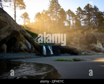 Raggi di sole che scendono lungo la scogliera sopra una cascata sulla spiaggia a Hug Point in Oregon Foto Stock