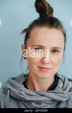 Primo piano ritratto di una donna con brillantini dorati sulle guance Foto Stock