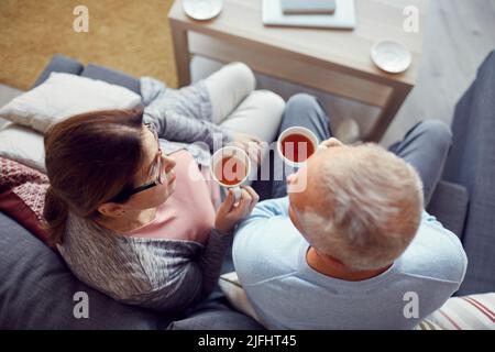 Direttamente sopra la vista della coppia anziana in abbigliamento casual seduto sul divano in soggiorno e bere il tè dalle tazze mentre si parla l'un l'altro Foto Stock