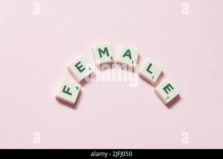 Femmina formata da piastrelle scrabble su sfondo rosa. Foto Stock