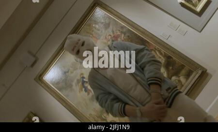 Un uomo in balaclava alla mostra d'arte vicino ai dipinti. Riprese. Concetto di vandalismo, uomo al museo d'arte. Foto Stock