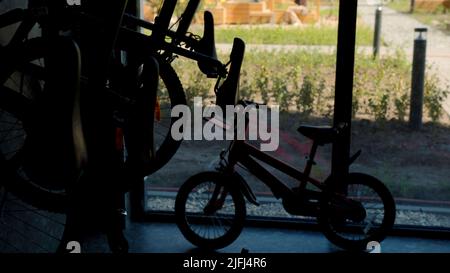 Parcheggio per biciclette all'interno dell'edificio con finestre panoramiche. Riprese in stock. Biciclette parcheggiate per bambini e adulti al coperto. Foto Stock