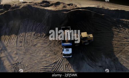 USA, California - 20 maggio 2022: Scavatore e caricamento della sabbia in camion di scarico a riva del fiume. Scena. Macchinari pesanti che lavorano in cava di sabbia. Foto Stock