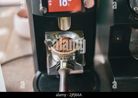 Macinare i chicchi di caffè versando in un portafiltro utilizzando una macchina per il caffè Foto Stock