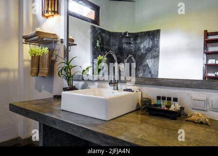 Bagno in hotel tropicale o casa residenziale. Interni di design con decor etnico, specchio e lavandino bianco nel resort Foto Stock