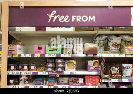 Un corridoio senza glutine con prodotti senza glutine sugli scaffali con un'agenzia pubblicitaria 'Free from' presso un supermercato Tesco a Basingstoke, Regno Unito Foto Stock