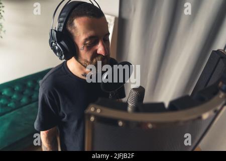 Giovane artista maschile europeo in cuffie registra le canzoni utilizzando il microfono closeup copy space . Foto di alta qualità Foto Stock