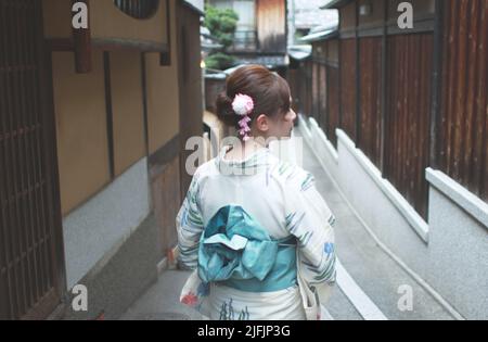 La parte posteriore di una donna giapponese, camminando su una vecchia strada stretta a Kyoto, Giappone indossando uno yukata Foto Stock