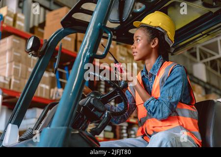 Donna nera africana lavoro di carico in magazzino personale di lavoro carrello elevatore a forche comando caricamento con radio prosciutto. Foto Stock