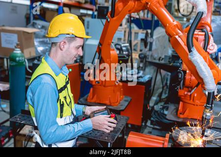 Il lavoratore che lavora con il braccio del robot automatizza la saldatrice nella moderna fabbrica di metallo. Programma di progettazione robotica nell'industria pesante. Foto Stock