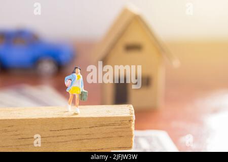 Persone in miniatura - Businesswoman borsa da trasporto in piedi sul pavimento di legno con auto blu sfocato e sfondo casa di carta. Concetto di viaggio e affari. Foto Stock