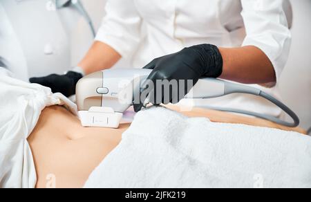 Primo piano osservare le mani del medico effettuando una procedura non invasiva di serraggio della pelle addominale, utilizzando un sensore con ultrasuoni micro-focalizzati spot strati di calore della pelle, fino a sistema muscoloaponeurotico SMAS. Foto Stock