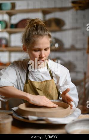 Un ceramista fa un piatto. Donna in grembiule lavora in un laboratorio di ceramica. Foto Stock