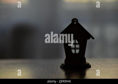 Una piccola casa di legno si erge su un tavolo a casa al buio, una casa per bambini per lo sfondo Foto Stock