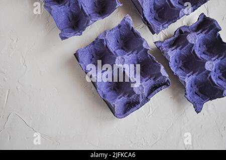 Vista dall'alto di cartoni vuoti di uova, di colore blu-viola, da riciclare, su sfondo bianco, scatole di uova Foto Stock