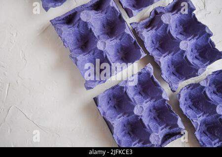 Vista dall'alto di cartoni vuoti di uova, di colore blu-viola, da riciclare, su sfondo bianco, scatole di uova Foto Stock