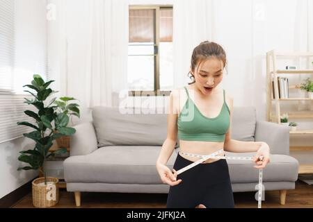 Concetto sano e di perdita di peso, giovane donna asiatica eccitata mentre misurando la vita con metro a nastro. Foto Stock