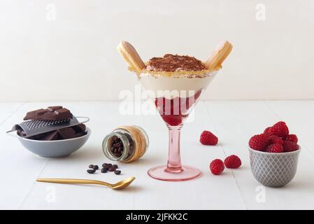 Tiramisù di lamponi fatto in casa veloce per una visita inaspettata, dolce senza torta dessert stile cheesecake con ingredienti posti su tavola bianca di legno. Foto Stock