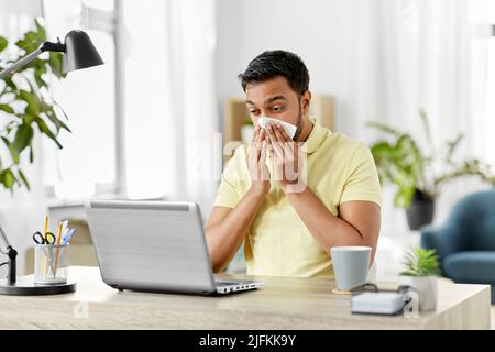 uomo indiano con il computer portatile che soffia il naso in ufficio Foto Stock