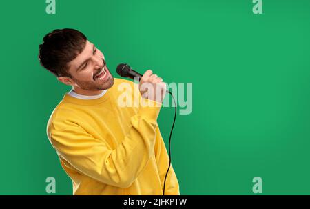 uomo in felpa gialla con microfono che canta Foto Stock