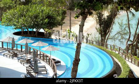 Lettini con ombrelloni o ombrelloni vicino alla splendida piscina nel moderno resort tropicale di lusso. Concetto di viaggio, viaggio e vacanza estiva in Foto Stock