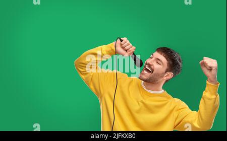 uomo in felpa gialla con microfono che canta Foto Stock