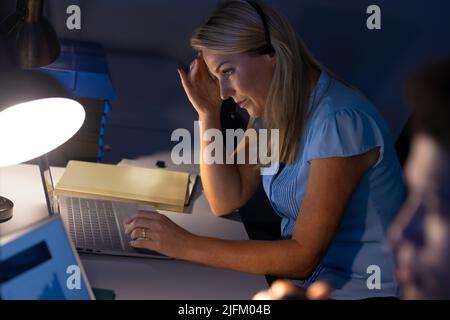 Vista ad alto angolo della donna d'affari caucasica con testa a portata di mano che lavora su un computer portatile sulla scrivania in ufficio Foto Stock