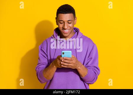 Ritratto di attraente ragazzo allegro messo a fuoco utilizzando il dispositivo chatting scrivere SMS isolato su sfondo di colore giallo vivo Foto Stock
