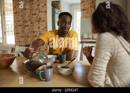 Il giovane uomo africano che versa il caffè per sua moglie durante la colazione Foto Stock