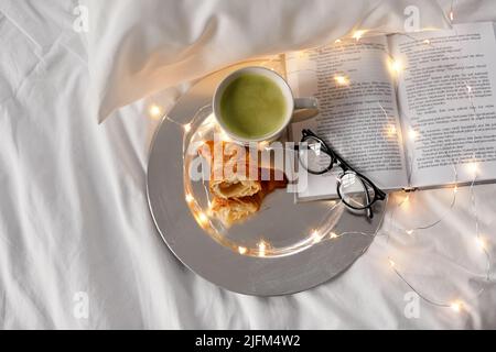 croissant, tè matcha, libro e bicchieri a letto Foto Stock